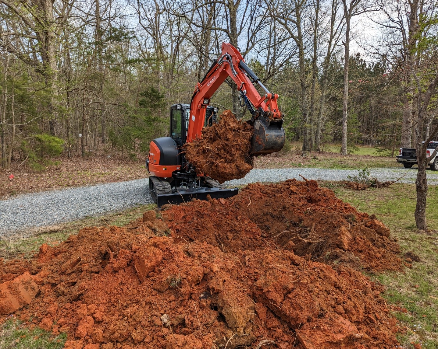 Mini excavator lifting a large stump and root ball during land clearing