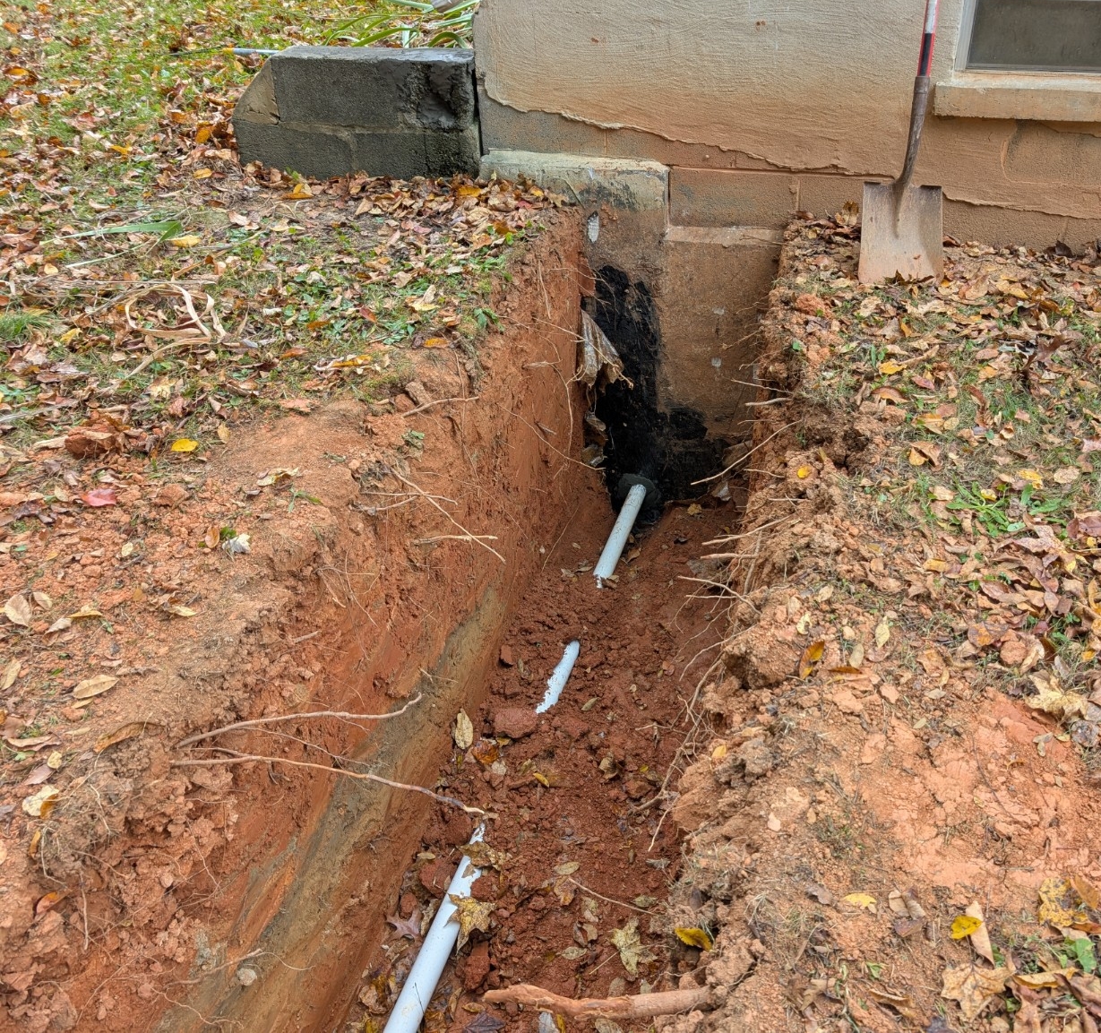 Trench excavation alongside a house foundation for underground drainage or utility work